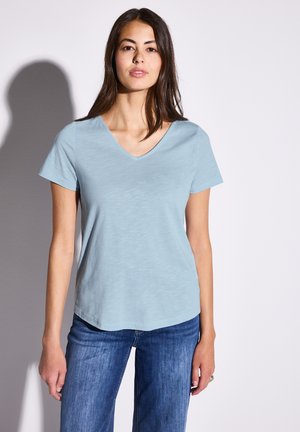 T-shirt azzurro chiaro con scollo a V realizzato in tessuto morbido, maniche corte e una vestibilità rilassata. Abbinato a jeans blu, con dettagli minimi visibili.