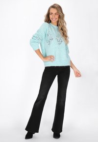 Jasnoniebieski sweter z dzianiny z diamentowymi wzorami i otwartymi detalami; w połączeniu z czarnymi dzwonami i czarnymi botkami.