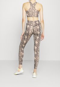 Sportovní podprsenka a legíny v béžovém a černém hadím vzoru, vyrobené z elastického materiálu, s designem racerback.