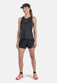 Top a maniche corte nera senza maniche e pantaloni corti blu navy, realizzati in tessuto leggero. Il modello indossa scarpe da ginnastica rosa e un cappellino nero.