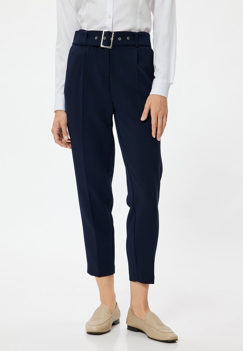 Marinblå högmidjade byxor med bälte och silverfärgad spänne, med veck, skräddarsydd passform och cropped längd. Matchas med beige ballerinaskor.