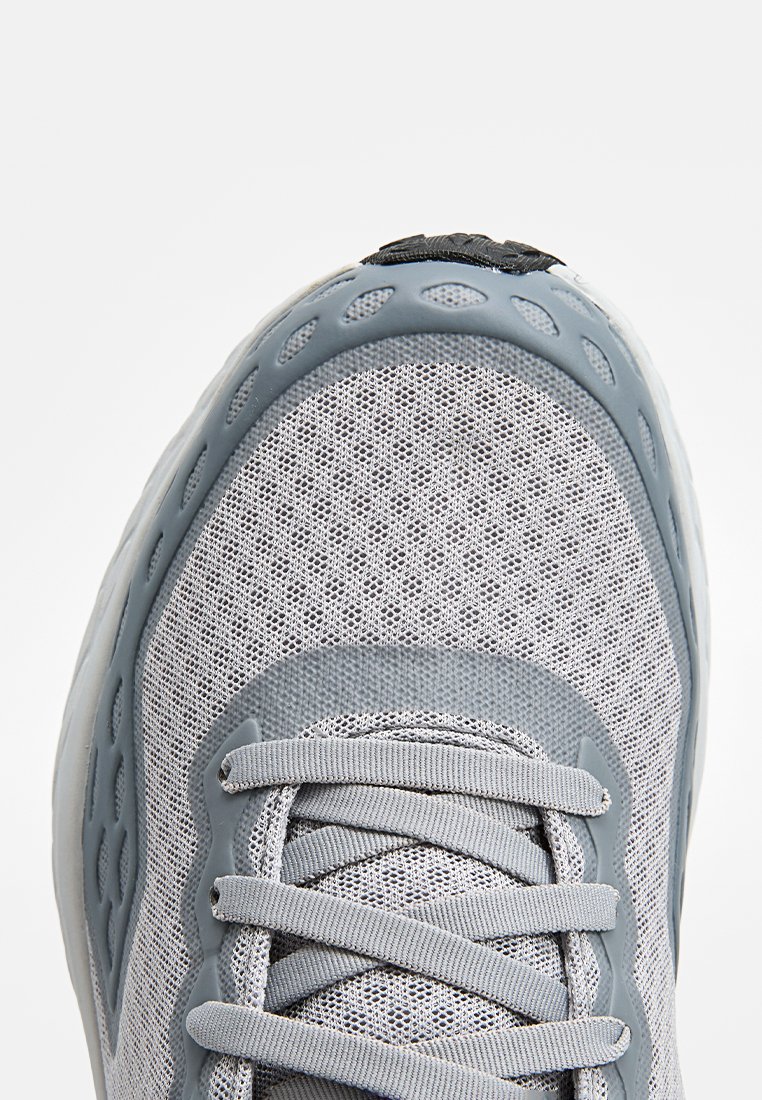 Graue Mesh-Sneaker mit einer strukturierten Oberseite, Gummisohle und flachen Schnürsenkeln. Auffällige abgerundete Kanten und Belüftungslöcher an den Seiten.