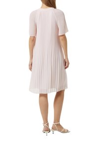 Lichtroze geplooide jurk met korte mouwen, ronde hals en vloeiende silouette, gecombineerd met witte sandalen met bandjes.