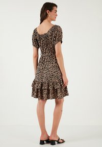 Leopard print dress featuring short sleeves, a ruffled hem, and a cinched waist. Made from soft fabric, in shades of brown and black.