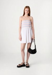 Šaty bez ramienok s naškrobeným vrchným dielom v pastelových pruhoch a bielou sukňou. Dopĺňajú ich čierne sandále na platforme a malá čierna kabelka.