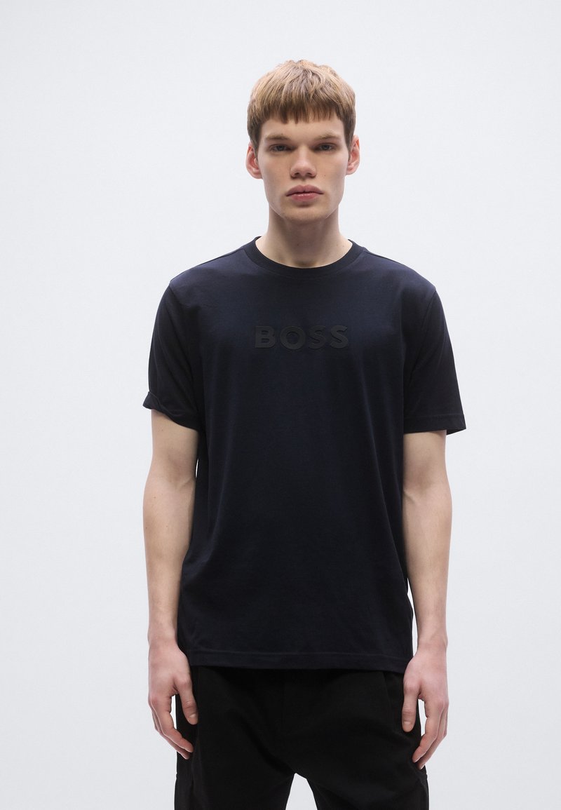 Fekete pamut póló klasszikus kerek nyakkivágással, rövid ujjakkal, és előoldalán dombornyomott "BOSS" logóval. Simább textúra és letisztult dizájn.
