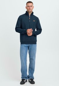 Mornarska zip-up jopica iz mehkega materiala, ki ima četrti zadrgo, stranske žepke, rebrasto manšeto in majhen usnjen logotip. Ujemite jo z modrimi kavbojkami.