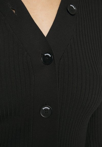 Mustaka ribbed knit kardigan V-kauluksella, jossa on kolme mustaa nappia, joista kahdessa on teksti "SANDRO". Teksturoitu kangas hienolla ribbaamisella.