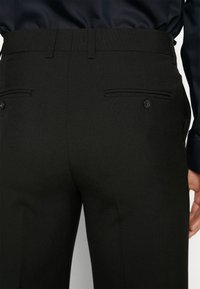 Fekete öltöny nadrág, testhezálló szabással, sima textúrával, két gombos hátsó zsebből és egyenes szárú fazonnal.