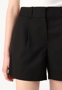 Svarta skräddarsydda shorts med platt midja, utrustade med sidofickor och en ren finish vid fållen, tillverkade av ett mjukt tyg.