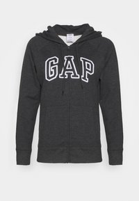 Sudadera con cremallera en gris, con capucha ajustable, bolsillos frontales y el logo de "GAP" en tela blanca. Textura suave con un corte holgado.