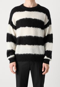 Sweter w czarno-białe paski o puszystej fakturze, z okrągłym dekoltem i opuszczonymi ramionami. Posiada wyraźne poziome paski oraz ściągacze przy rękawach.