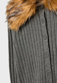 Siv pulover s rebrastim vzorcem in rjavim krznenim ovratnikom, ki ima spredaj šest črnih gumbov. Tekstura tkanine povečuje njegovo vizualno privlačnost.