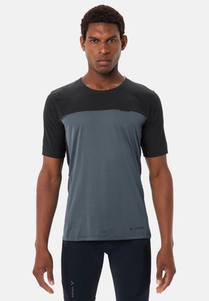 Mann steht frontal mit einem kurzärmeligen schwarzen und grauen Sportshirt und schwarzen Radhosen mit Logos.