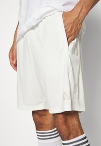 Pantalones cortos deportivos blancos que cuentan con un material suave y ligero, con bolsillos laterales y un sutil detalle de logo en el dobladillo. Combinados con calcetines a rayas.