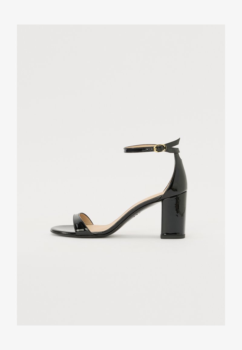 Sandale en cuir verni noir avec un large talon, orteils ouverts et une bride de cheville ornée d'une boucle en or. Texture lisse et design épuré.