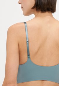 Eine Rückansicht eines hellblauen BHs mit dünnen, glänzenden Trägern und einem glatten, nahtlosen Design. Er hat einen einfachen, runden Schnitt.