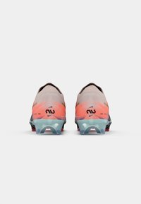 Buty piłkarskie o gradientowym wzorze w odcieniach brzoskwini do różu, z teksturowaną syntetyczną cholewką oraz czarnymi akcentami na pięcie i logo.