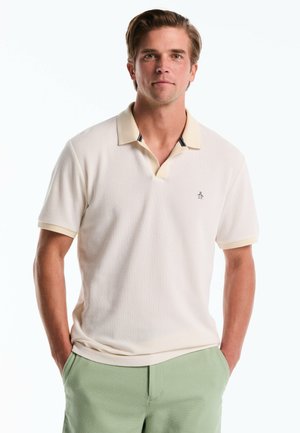 Crèmekleurige polo met een gestructureerde stof, voorzien van een v-hals kraag met lichtgele bies en donkere accenten. Klein logo op de borst.