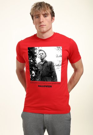 Rød bomulds t-shirt med et sort-hvidt grafisk motiv af en maskeret figur, med teksten "Alle har ret til en god skræmtoplevelse" nedenunder.