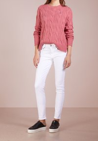 Pull en maille torsadée rose avec col rond, associé à un jean blanc ajusté et des chaussures noires à enfiler avec fermeture éclair.