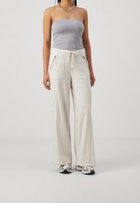 Kapsáčové kalhoty s širokými nohavicemi v krémové barvě, vyrobené z lehkého materiálu. Mají dvě přední kapsy, pás s šňůrkou a volný střih.