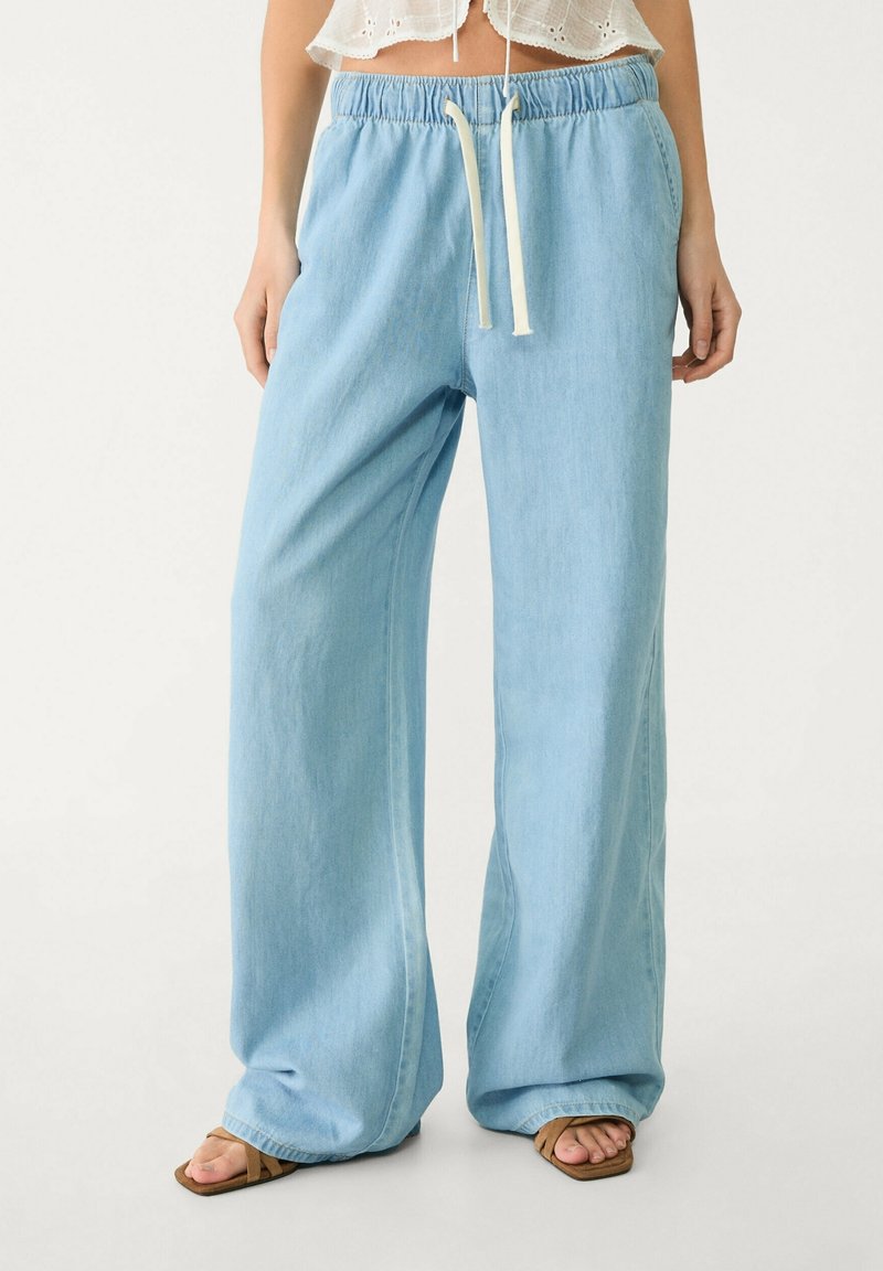Pantaloni larghi di colore azzurro chiaro realizzati in denim morbido, con vita elastica e coulisse regolabile; vestibilit�à rilassata, con orli a gambale.