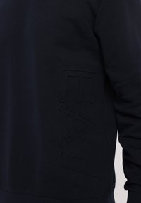 Sweatshirt azul marinho com um logótipo texturizado no lado esquerdo, feito de tecido macio com um acabamento suave e um corte descontraído.