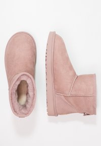 Botines de ante rosa con forro interior esponjoso, suelas de goma planas y costuras visibles, mostrados desde ángulos superior y lateral sobre fondo blanco.