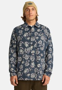 Marineblauw bloemenoverhemd met lange mouwen van katoen, voorzien van een button-down kraag, een voorkeurszak en ingewikkelde lichtgekleurde bloemenpatronen.