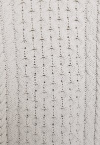 Tessuto lavorato a maglia in un colore beige chiaro, caratterizzato da un motivo testurizzato con cavi attorcigliati e punti aperti, creando un aspetto morbido e invitante.