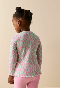 Bluza cu mâneci lungi din material cu nervuri, având un model zigzag în roz, verde și alb. Prezintă margini ondulate și decolteu rotund.