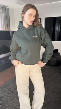 Sweat à capuche court vert olive avec logo sur la poitrine, accompagné d'un pantalon ample beige. Tissu doux, coupe décontractée, détails de couture visibles.