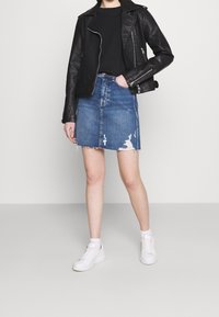 Zwarte neplederen motorjack, gecombineerd met een blauwe denim rok met rafelige zoom en slijtage. Witte sneakers maken de outfit compleet.