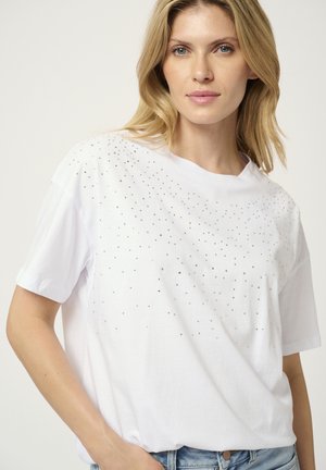 T-shirt en coton blanc avec une coupe décontractée, des manches courtes et des clous en argent parsemés sur le devant pour ajouter de la texture et du détail.