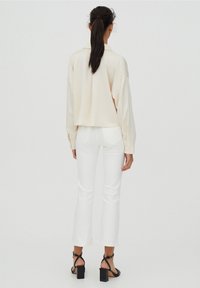 Camicia oversize color crema con colletto, abbinata a jeans flare bianchi e sandali neri con tacco. Tessuto morbido; dettagli minimi.