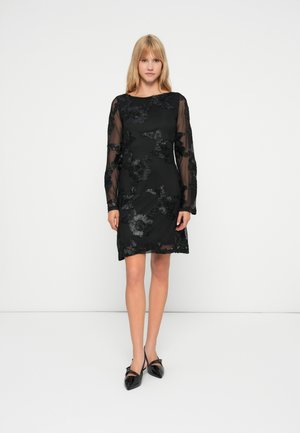 Robe noire avec des manches longues en voile transparent, ornée de broderies florales noires et d'un col rond. Texture lisse et coupe courte, ample.