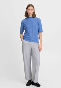 Blauer, gestrickter Kurzarmpullover mit einem strukturierten Muster, kombiniert mit hellgrauen, weiten Hosen und schwarzen Schuhen.