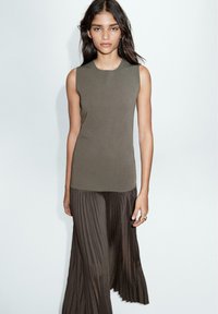 Ärmelloses olivfarbenes Top aus glattem Stoff kombiniert mit einem dunklen, plissierten Rock, der eine subtile Textur und ein fließendes Design aufweist.