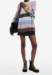 Pull en maille multicolore avec des rayures horizontales aux couleurs pastel, associé à une mini jupe noire et des bottines marron. Sac à bandoulière ajustable.