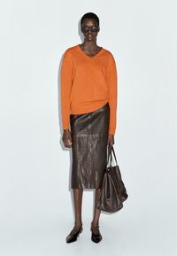 Orange v-neck sweater, brown leather midi skirt, black pointed flats, and a brown tote bag. Smooth textures and fitted silhouette.