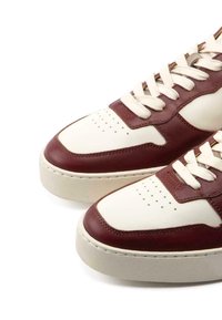 Weiße und burgunderfarbene Leder-Sneaker verfügen über eine perforierte Zehenbox, eine gepolsterte Zunge, flache beigefarbene Schnürsenkel und eine strukturierte Gummisohle.