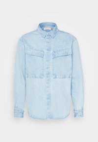 Light blue denim shirt with a button-down collar, two chest pockets, long sleeves, and a straight hem. Features subtle texture and stitching details.