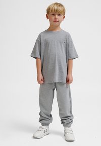 Grå bomulds T-shirt med korte ærmer og et lille sort logo, parret med matchende grå joggers og hvide sneakers med stropper.