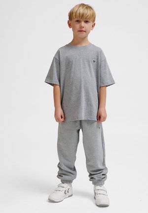 Grå bomulds T-shirt med korte ærmer og et lille sort logo, parret med matchende grå joggers og hvide sneakers med stropper.