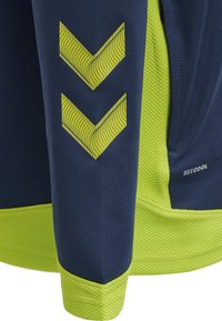 Top sportivo in navy e verde lime con finitura testurizzata. Presenta strisce a zigzag in materiale riflettente sulla manica. Realizzato in tessuto traspirante.
