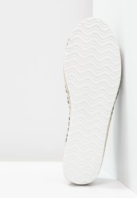 Semelle de chaussure blanche avec une texture ondulée, arborant des accents beiges sur les côtés et un tissu à motifs s'étendant sur les côtés.