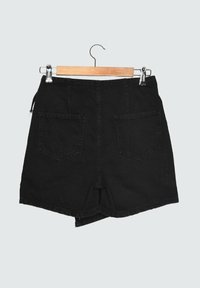 Mustat farkkushortsit, joissa on korkea vyötärö, takataskut ja reunatiedot. Roikkuu puu-hengarissa vaaleaa taustaa vasten.