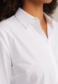 Vit skjorta med knäppning framtill som har en klassisk krage, mjukt bomullstyg och subtila sömnadsdetaljer. Inkluderar en bröstficka.