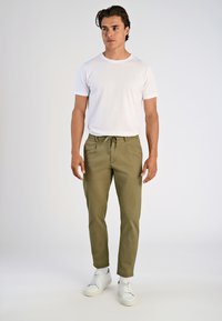 Witte crew neck t-shirt gecombineerd met olijfgroene joggingbroek met trekkoord. Model draagt witte sneakers en toont een casual outfit.